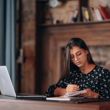 A woman's hand writing down on a white blank notebook on table.
